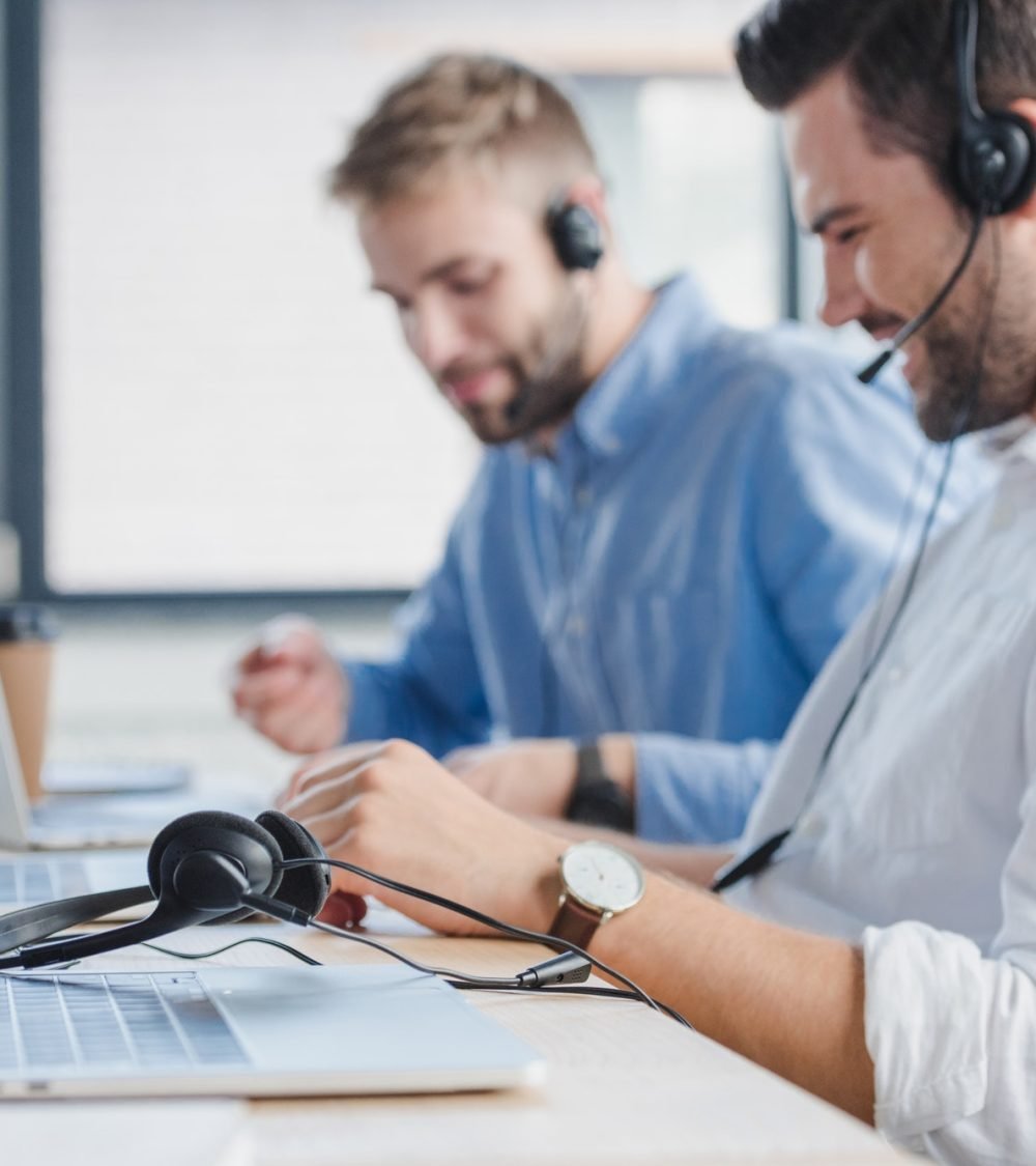 smiling-young-call-center-operators-in-headsets-using-laptops-in-office.jpg